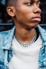 Crop black trendy serious male with silver chain on neck in blue denim jacket looking away on street — Stock Photo