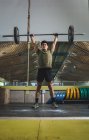 Сосредоточенный азиатский спортсмен делает тягу с тяжелой штангой во время тренировки в спортзале, отводя взгляд — стоковое фото