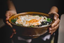 Mani di persona anonima in possesso di ciotola di zuppa con tagliatelle e uova — Foto stock