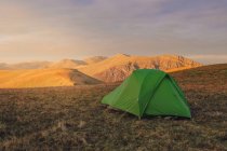 Tenda de acampamento verde colocada em colina gramada em terras altas ao pôr do sol no País de Gales — Fotografia de Stock