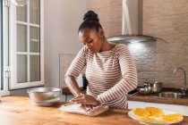 Junge Afroamerikanerin zerkleinert frischen Kochbananen auf Schneidebrett, während sie zu Hause Patacones zubereitet — Stockfoto