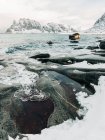 Acqua fredda del mare spruzzata sulle rocce vicino alla costa ghiacciata e innevata vicino alle montagne nella grigia giornata invernale sulle Isole Lofoten, Norvegia — Foto stock