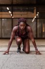 Femme sportive afro-américaine confiante debout sur le début accroupi préparé pour courir dans la rue — Photo de stock