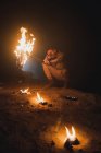 Aventurero masculino irreconocible con antorcha ardiente brillante agachándose mientras explora la cueva subterránea oscura durante la expedición de espeleología - foto de stock