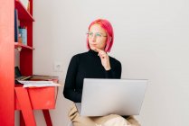 Giovane freelance femminile concentrata in abiti casual seduta sulla sedia e utilizzando il computer portatile mentre si lavora sul progetto in leggero appartamento moderno — Foto stock