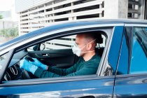 Side view of serious man using a protective mask driving car during quarantine time — Stock Photo