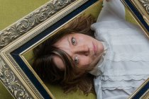 Top view of young long haired female with green eyes dressed in white blouse looking at camera through ornamental picture frame — Stock Photo