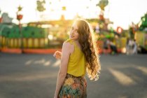 Encantada mulher de pé olhando para a câmera no parque de feiras e desfrutando de fim de semana de verão durante o pôr do sol — Fotografia de Stock