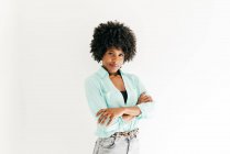 Glückliche junge Afroamerikanerin mit schönen Afrohaaren im trendigen Outfit, die in die Kamera auf weißem Hintergrund blickt — Stockfoto
