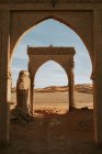 Arc de vieux bâtiment en ruine situé dans un désert sablonneux contre un ciel nuageux par temps ensoleillé près de Marrakech, Maroc — Photo de stock