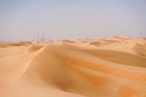 Paisagem desértica minimalista com dunas de areia e céu azul claro na Emirates. Torres de transmissão à distância. — Fotografia de Stock