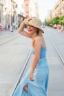 Side view of cheerful female in straw hat and summer clothes standing in street and enjoying summer day in city — Stock Photo