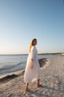 Femme blonde aux cheveux longs debout sur la plage regardant au loin — Photo de stock