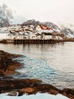 Mar frío con aguas tranquilas cerca de asentamientos costeros y cumbres nevadas en un día nublado de invierno en las Islas Lofoten, Noruega - foto de stock