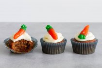 Rangées de délicieux cupcakes aux carottes sucrées à la crème tendre et aux gommes en forme de carotte sur une surface grise — Photo de stock
