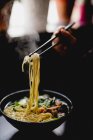 Main de femme méconnaissable cueillette de nouilles avec des baguettes de bol de soupe asiatique salée dans le café — Photo de stock