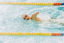 Vista lateral del deportista paralímpico con gafas y gorra sin estilo de natación a mano en la piscina entre carriles - foto de stock