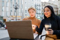 Joyeux freelance multiracial assis à table avec ordinateur portable et travaillant sur un projet à distance ensemble dans un café en plein air — Photo de stock