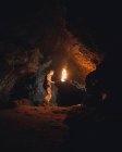 Вид збоку молодого чоловіка спелеолог з палаючим факелом, що стоїть у темній вузькій скелястій печері, досліджуючи підземне середовище — стокове фото