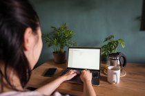 Back view of unrecognizable Asian female freelancer reading documents on laptop while sitting at table during remote work — Stock Photo