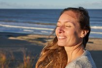 Транквіль Жінка з закритими очима насолоджується заходом сонця влітку на пляжі біля моря — стокове фото
