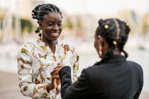 Modische lächelnde Afroamerikanerinnen, die bei strahlendem Sonnenschein Zeit miteinander verbringen und sich im Park die Hände reichen — Stockfoto