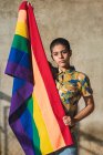 Серйозна молода бісексуальна жінка з різнокольоровим прапором, що представляє ЛГБТ-символи і дивиться на камеру в сонячний день. — стокове фото
