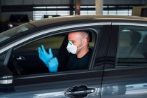 Side view of serious man using a protective mask putting on gloves driving car during quarantine time — Stock Photo