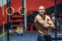 Мускулистый бородатый мужчина смотрит в сторону, стоя рядом с оборудованием во время тренировки в современном тренажерном зале — стоковое фото