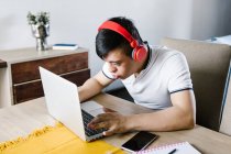 Focus Latin teen boy with Down syndrome browsing netbook while sitting at table and studying online from home — Stock Photo