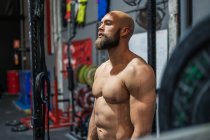 Muscular bearded man looking away while standing near equipment during workout in modern gym — Stock Photo