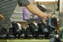 Detalle de las manos del hombre mientras revisa los zapatos en la línea de producción de control de calidad en la fábrica de zapatos chinos - foto de stock