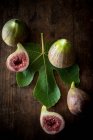 Vue de dessus de figues mûres coupées en deux et entières placées avec des feuilles vertes sur une table rustique en bois — Photo de stock