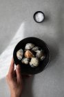 Вид зверху на обрізану невпізнавану людину, що тримає миску з невареними молюсками та сіллю, поміщеною на сірому столі під час приготування їжі — стокове фото