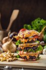 Hambúrgueres apetitosos com legumes colocados em tábua de madeira com batatas fritas na cozinha — Fotografia de Stock