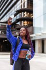 Cheerful muscular African American sporty woman taking selfie with energy drink on street — Stock Photo