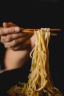 Hand of woman holding bamboo chopsticks with tasty wheat noodles from Chinese ramen meal plate — Stock Photo