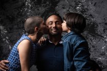 Femme aimante multiethnique et fils adolescent embrassant l'homme sur la joue sur fond sombre en studio — Photo de stock