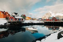 Quay nevado em pacífico assentamento costeiro com casas vermelhas no dia nublado de inverno nas Ilhas Lofoten, Noruega — Fotografia de Stock