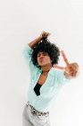 Jeune femme afro-américaine ludique en tenue tendance s'amusant et montrant signe de paix sur fond blanc — Photo de stock