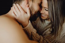 Alegre joven hombre y mujer sonriendo y abrazándose mientras yacen en la cómoda cama en casa juntos - foto de stock