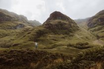 Back view of unrecognizable man standing on rough grassy hillside during trip through Glencoe in the UK countryside on cloudy day — Stock Photo