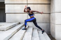 Vista laterale della forte donna afroamericana che corre su per le scale mentre si allena vicino all'edificio moderno sulla strada della città — Foto stock