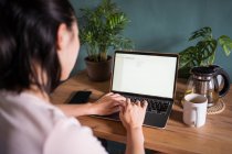 Visão traseira do freelancer asiático irreconhecível lendo documentos no laptop enquanto se senta à mesa durante o trabalho remoto — Fotografia de Stock