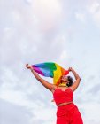 From below of stylish African American female in trendy wear raising flag with rainbow ornament while looking away on roadway — Stock Photo