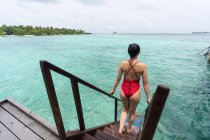 Back view of anonymous female in swimsuit going down on stairs into water relaxing in Maldives — Stock Photo