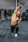 Full body shirtless bearded guy looking away stretching elastic band with arms and lunging during functional workout in gym — Stock Photo