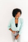 Heureuse jeune femme afro-américaine avec de beaux cheveux afro en tenue tendance regardant loin sur fond blanc — Photo de stock