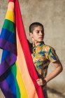 Grave giovane donna etnica bisessuale con bandiera multicolore che rappresenta i simboli LGBTQ e distoglie lo sguardo nella giornata di sole — Foto stock