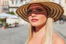 Vista lateral de la encantadora mujer con sombrero de paja mirando hacia otro lado en el día soleado en la calle de la ciudad en verano - foto de stock